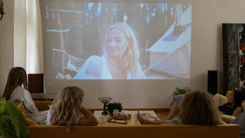 Pasangan muda sedang belajar bahasa Inggris dengan cara menonton film dengan subtitle bahasa Inggris di rumah pada hari Sabtu yang santai, menggambarkan metode belajar yang menyenangkan.