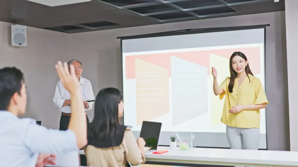 Seorang pembicara profesional sedang membuka presentasi bahasa Inggris dengan penuh percaya diri di depan audiens, menunjukkan teknik public speaking yang efektif.